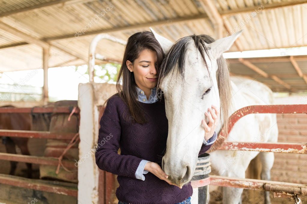 Loving mid adult woman feeding horse while standing in stable
