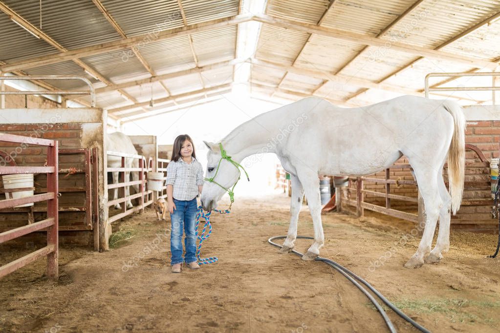 Full length of little rancher standing with white horse in stable