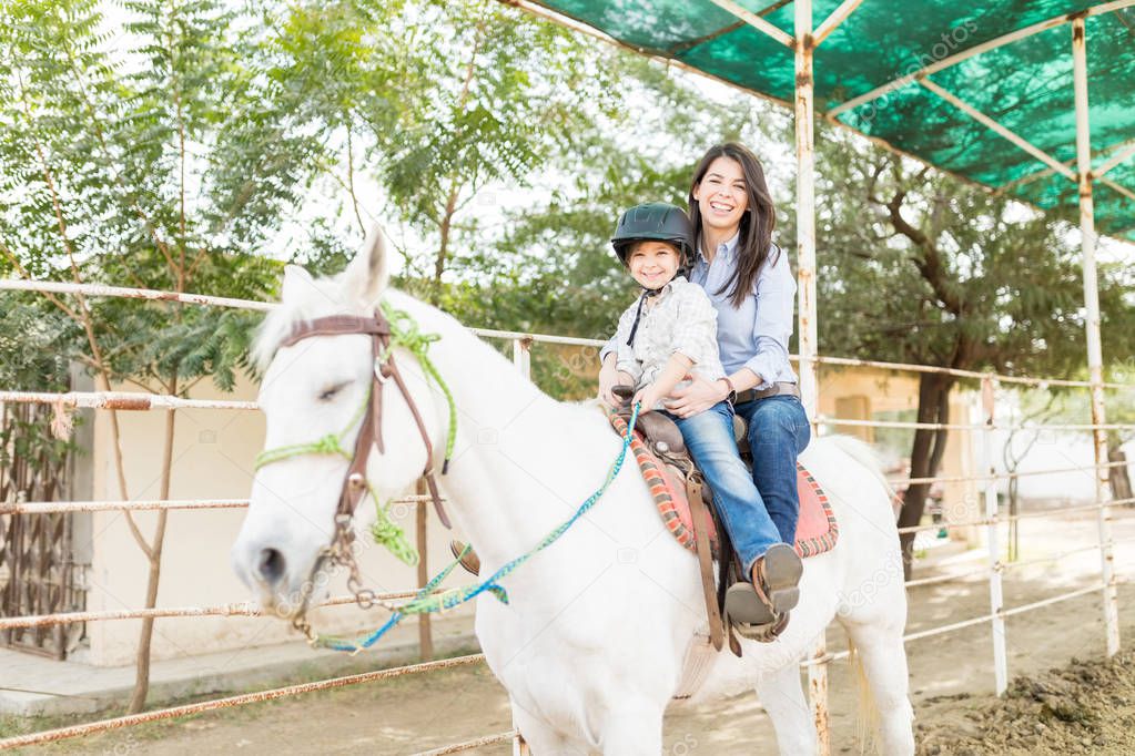 Portrait of happy mother and daughter riding white horse at farm