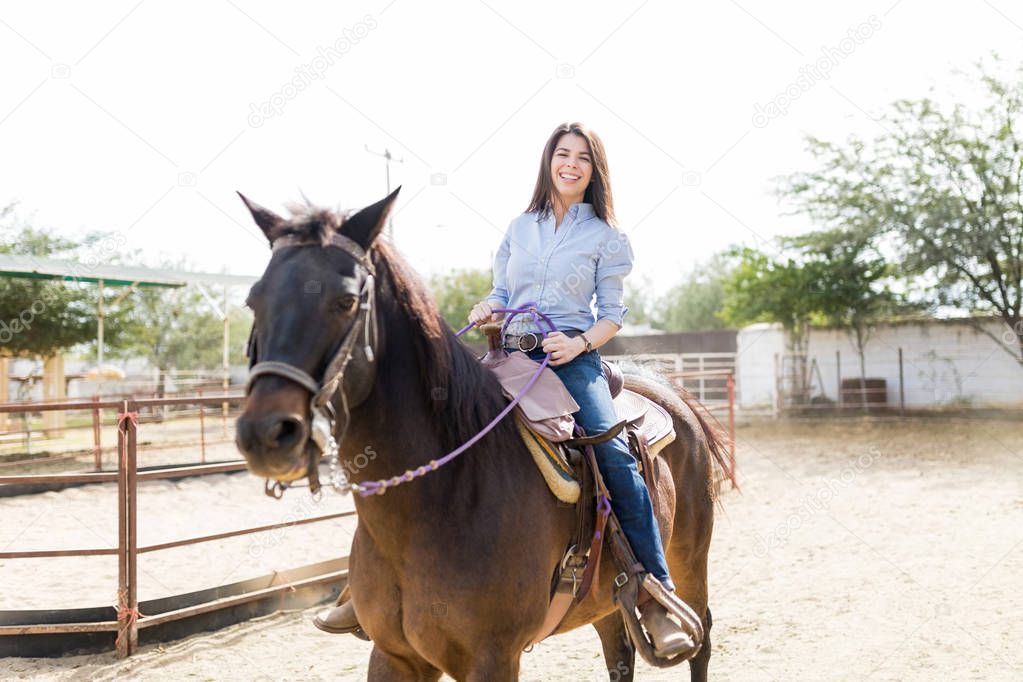 Portrait of happy and confident female jockey riding horse at barn