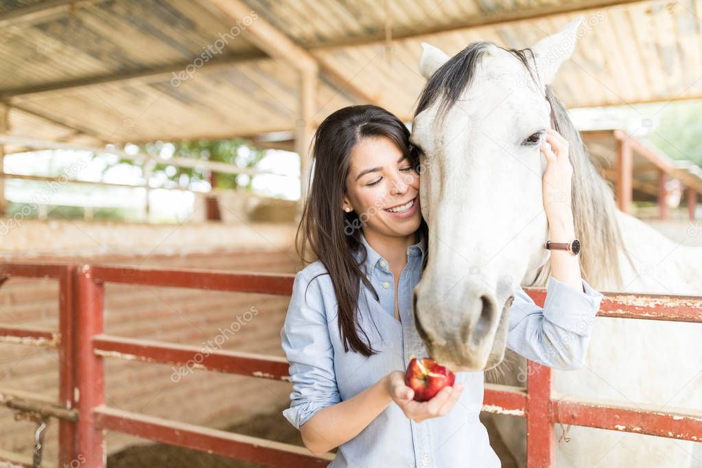 Smiling mid adult woman feeding fresh apple to horse at stable