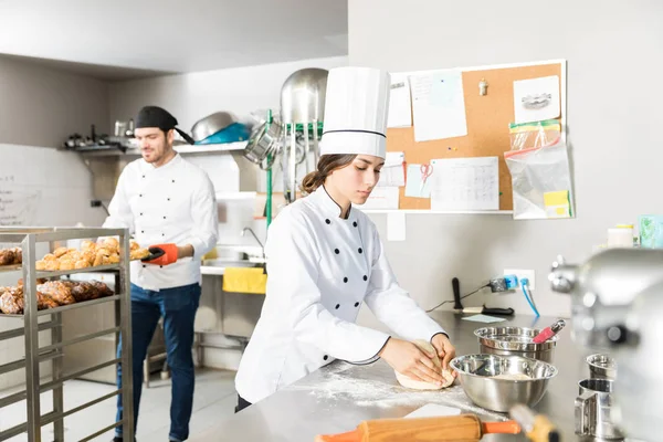 Female Chef Kneading Dough While Colleague Removing Fresh Bread Rack — Stock Photo, Image