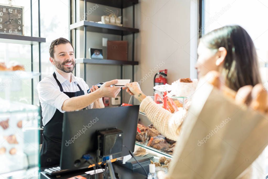 Happy salesman receiving credit card from customer in bakery