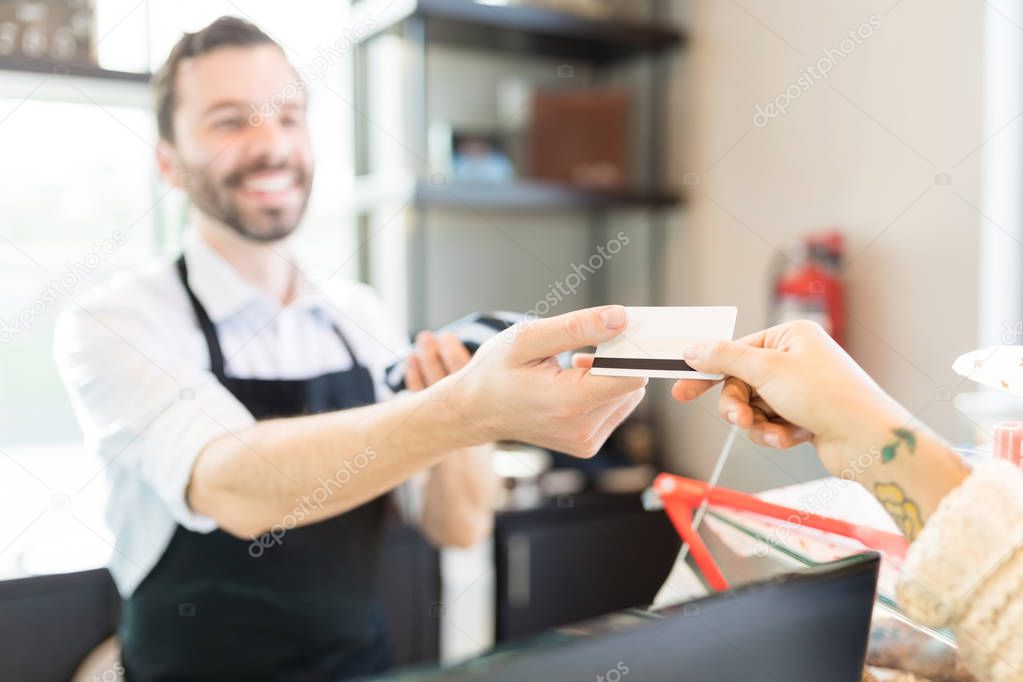 Hands of salesperson and client passing credit card for payment in bakery