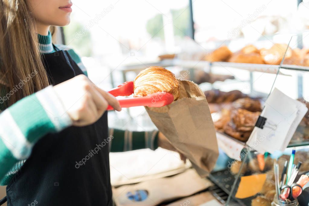 Midsection of female baker packing freshly baked croissant in shop