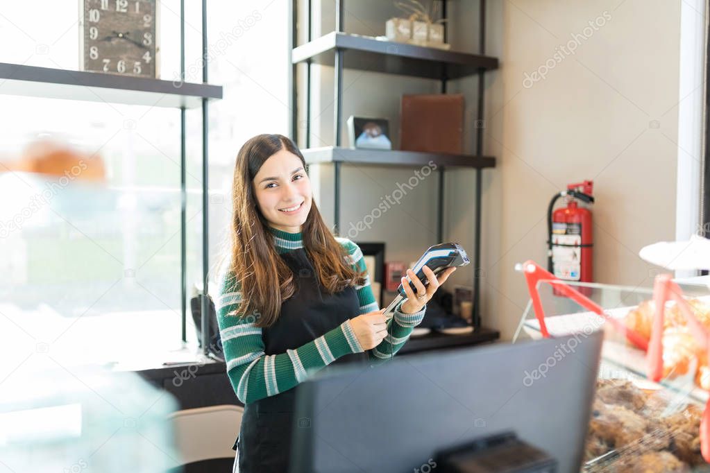 Portrait of content salesgirl holding credit card and reader in bakery