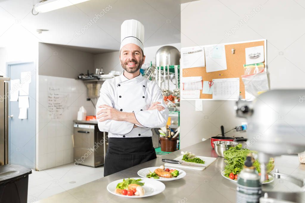 Mid adult chef smiling while crossing arms at kitchen counter