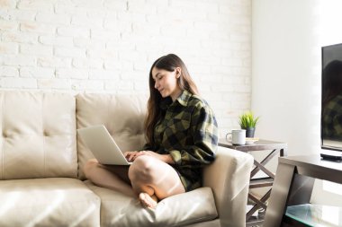 Evde kanepede dinlenirken dizüstü bilgisayar kullanan İspanyol kadın