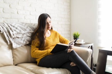 Young brunette woman reading novel on sofa in living room