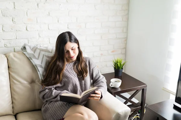 Relaxed woman smiling while reading novel on weekend morning