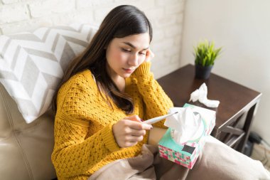 Genç kadın vücut ısısını termometre oturma odasında üzerinde ölçüm 