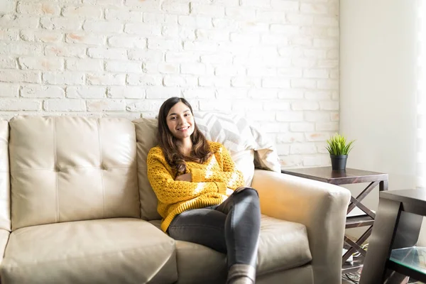 自宅のソファーで休んで自信の表情で居心地の良い黄色いセーターの女性の肖像画 — ストック写真