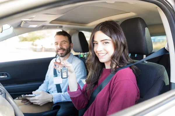 Good looking woman showing car keys while instructor smiling during driving class