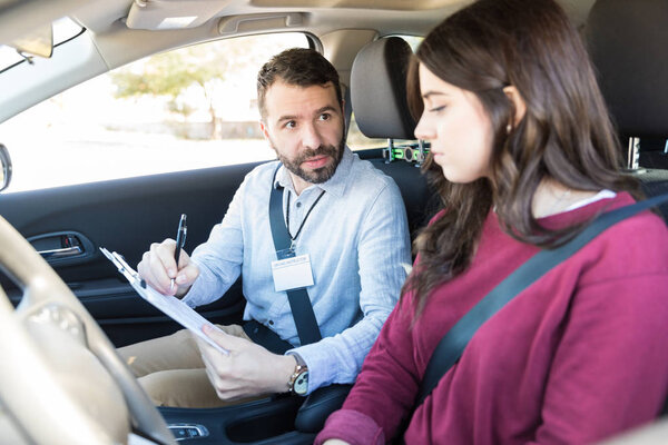 Confident driving examiner showing driving details to learner sitting in car