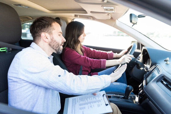 Handsome teacher gesturing while teaching car driving to female learner