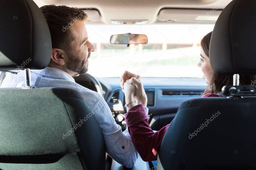 Rear view of romantic man and woman holding hands while sitting in car