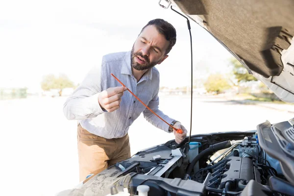 Good looking man checking level of engine oil in the car on street