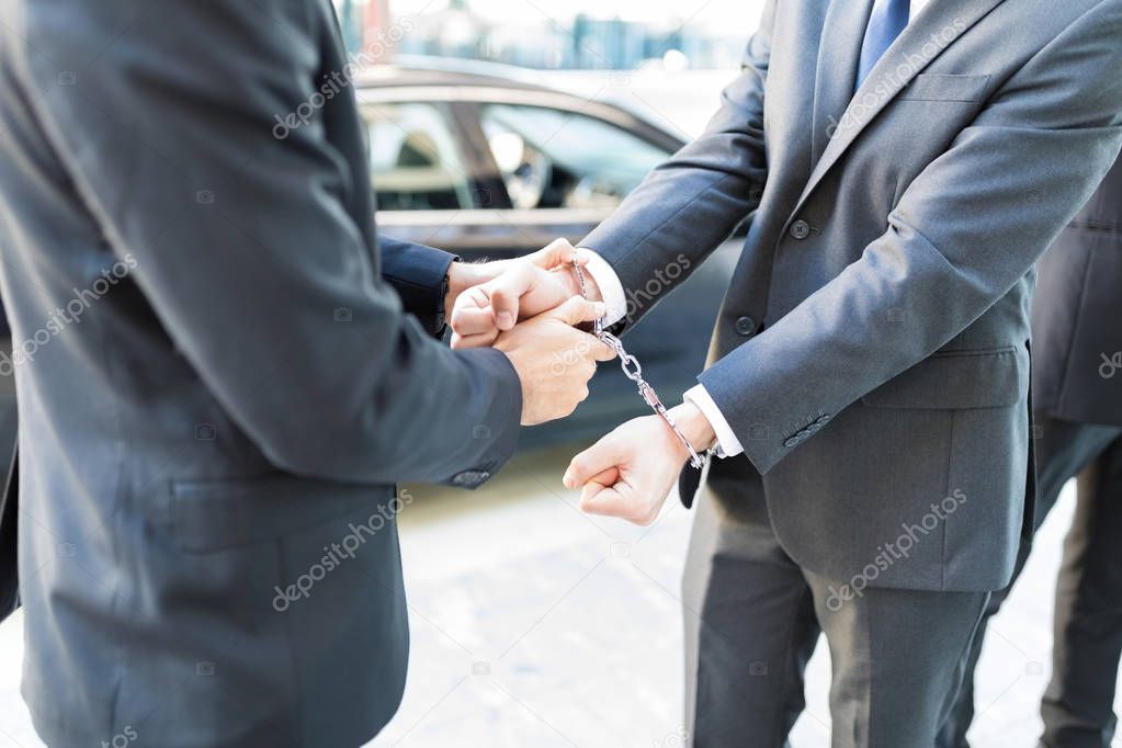 Midsection of undercover agent handcuffing corrupt entrepreneur