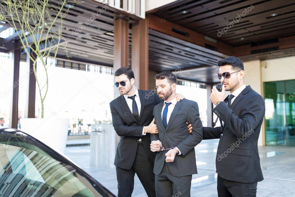 Male secret agents with corrupt politician walking towards car outside office building