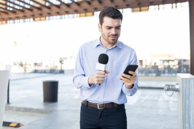 Yakışıklı muhabiri mike açık havada tutarak Smartphone kullanarak