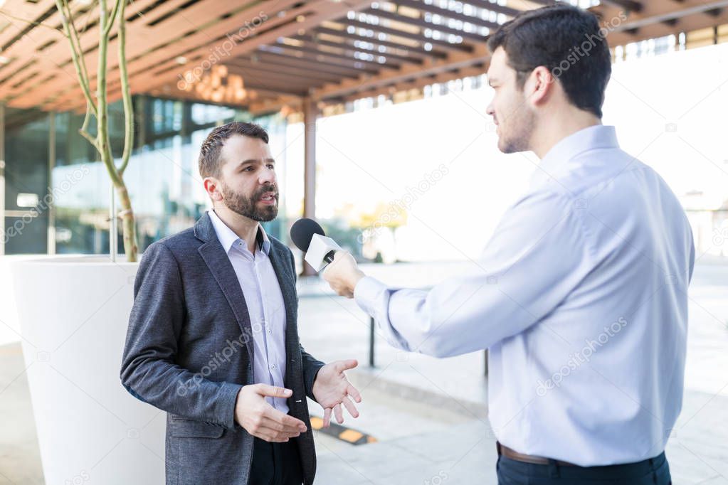 Mid adult famous personality wearing suit and giving interview to broadcaster outdoors