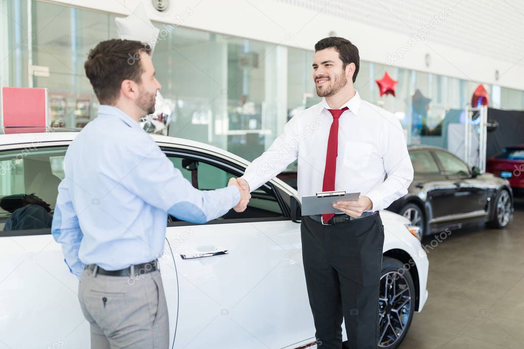 Smiling sales expert welcoming mid adult customer in car showroom