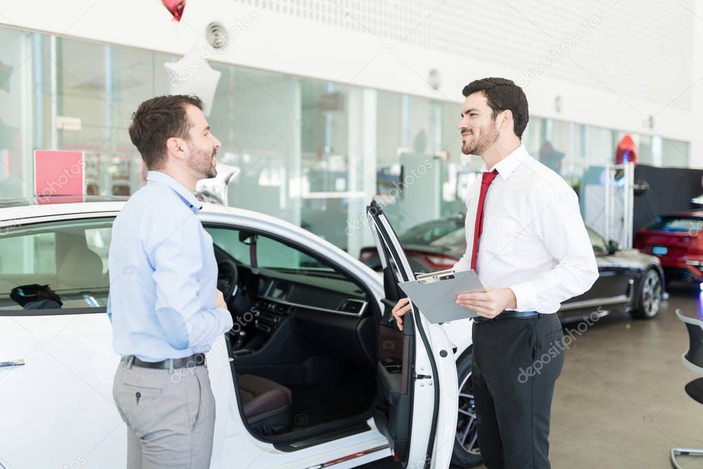 Confident sales expert showing new car to businessman in showroom