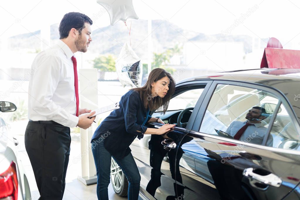 Mid adult woman checking out car before purchasing it from dealer in salon
