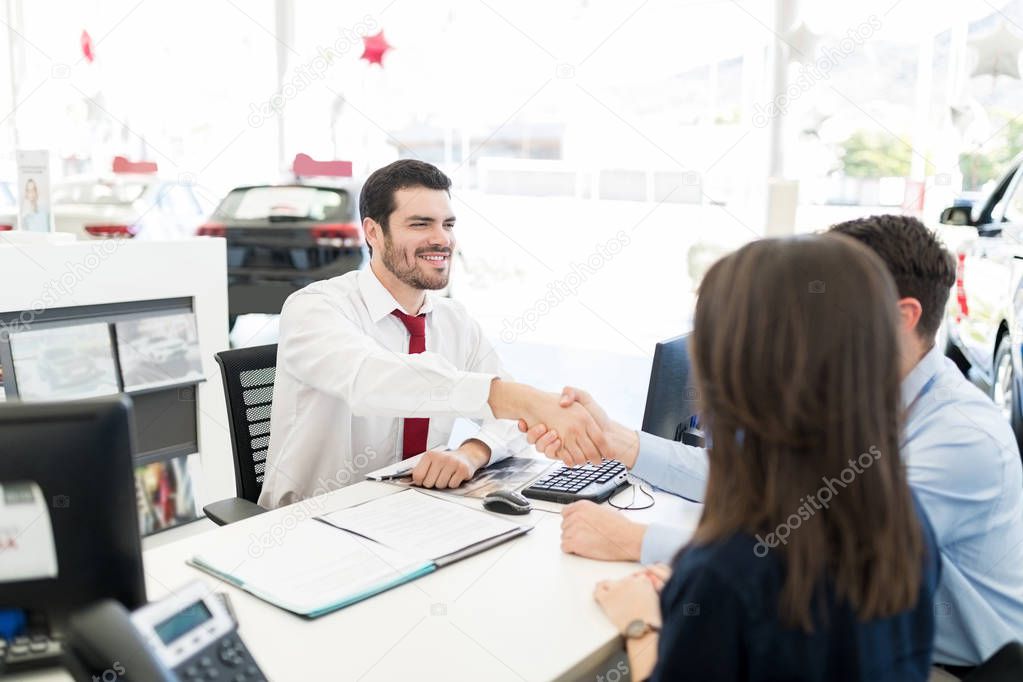 An attractive sales expert congratulating couple with a handshake at dealership