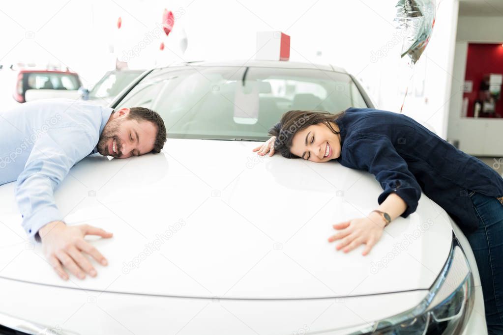 Content Hispanic couple embracing their newly purchased car in automobile salon