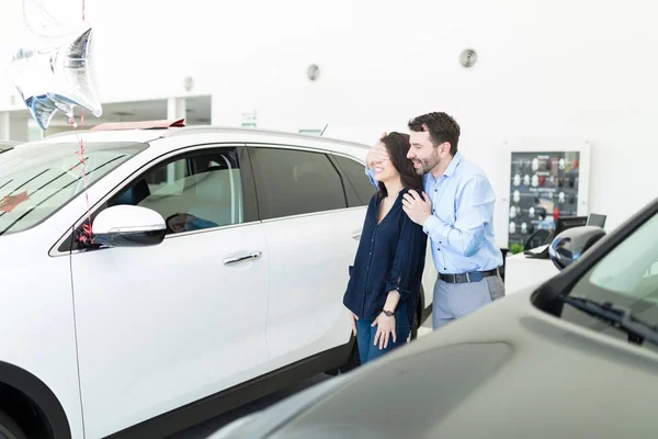 Mid adult boyfriend covering woman\'s eyes to give her a surprise in car dealership