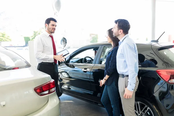 Sales representative explaining pros and cons of brand new car at dealership — Stock Image Sales Representative Explaining Pros Cons Brand New Car Dealership Royalty Free Stock Photos