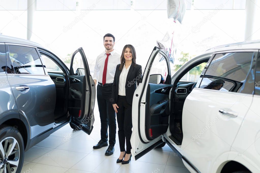 Lunghezza completa dei commercianti professionisti di bell'aspetto che aprono le porte delle automobili allo showroom