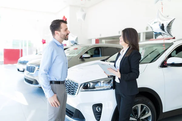 Showroom employee offering best lease deal to customer while standing by luxury cars