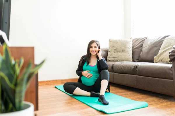 穿着运动装的妇女坐在健身垫上 在她怀孕期间在家里 — 图库照片