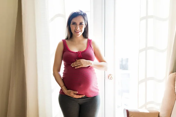 Retrato Una Mujer Bonita Protegiendo Vientre Embarazada Mientras Sonríe Casa —  Fotos de Stock