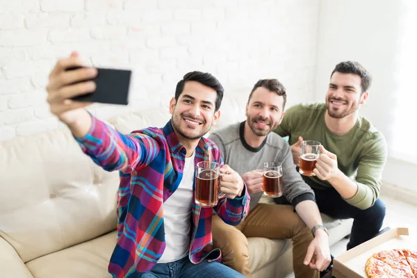 家でビールを持ちながら Selfie を取って笑顔のハンサムな男性の友人 — ストック写真
