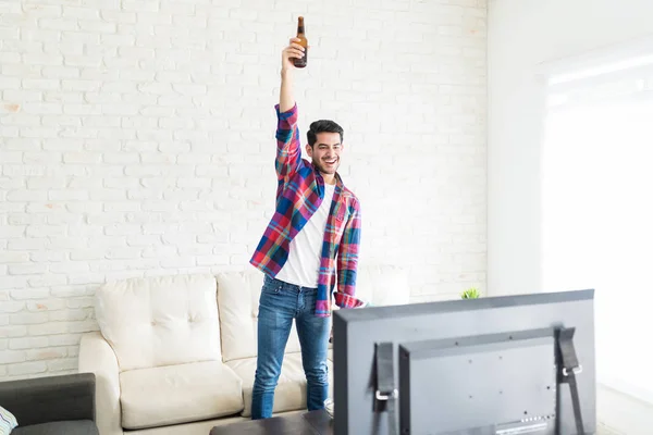 Возбужденный Привлекательный Мужчина Поднимает Бутылку Пива Празднует Победу Своей Любимой — стоковое фото