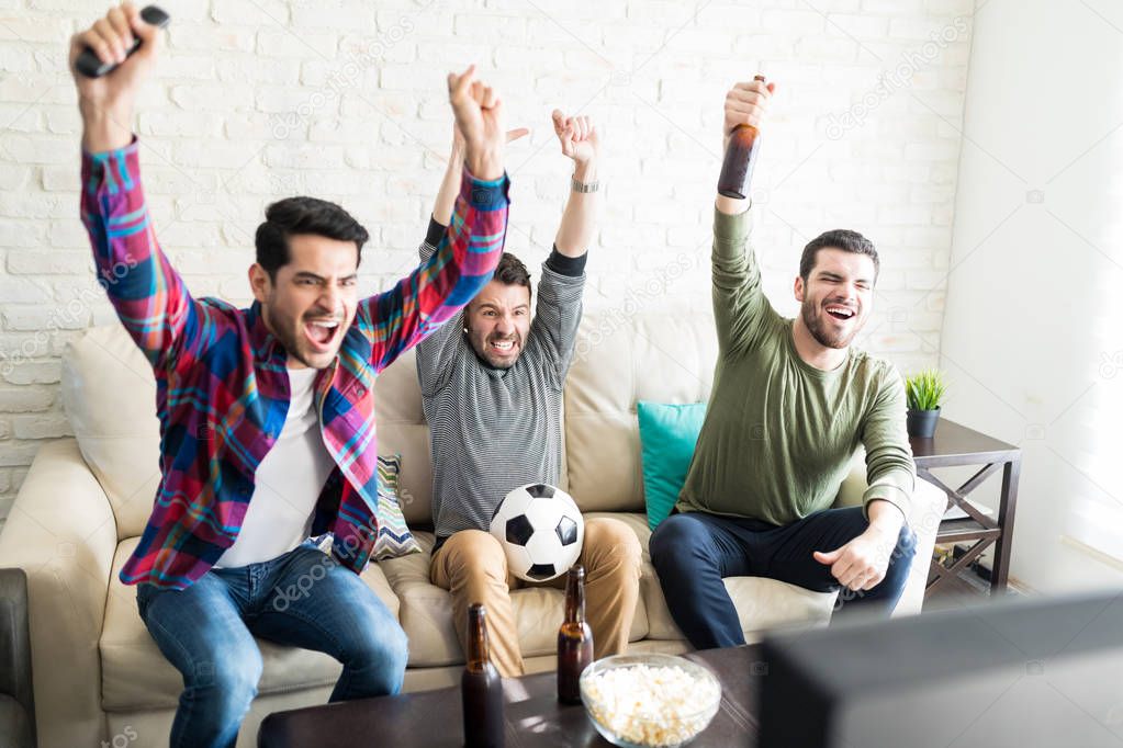 Hispanic male buddies celebrating goal and screaming in front of television at home