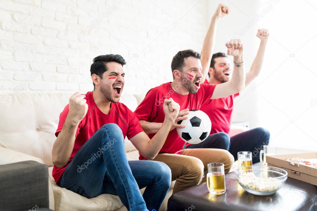 Overjoyed friends with soccer ball showing their uncontrollable joy at home