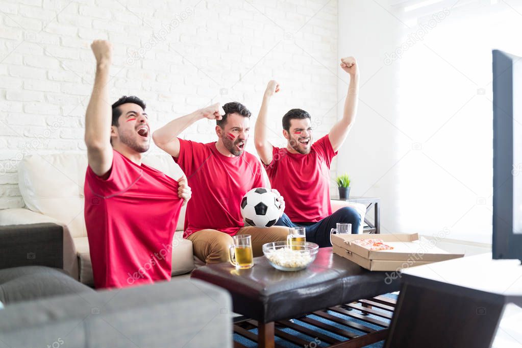 Proud soccer fans cheering while hanging out together to watch match at home