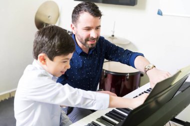 Erkek eğitmen elektrikli piyano Müzik Okulu oynarken müzik notları okumak için çocuk öğretmek