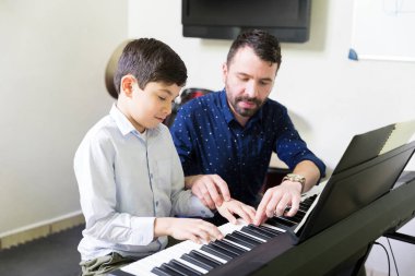 Küçük öğrenci ses synthesizer müzik akademisinde oynamak için öğrenme yardımcı erkek eğitmen