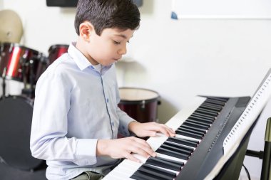 Kendine güvenen erkek öğrenci Müzik Okulu elektrik piyano çalmayı öğrenme