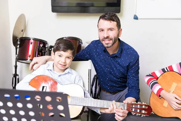 音楽の授業でギターの基本的な曲を再生する少年を助ける家庭教師の肖像 — ストック写真