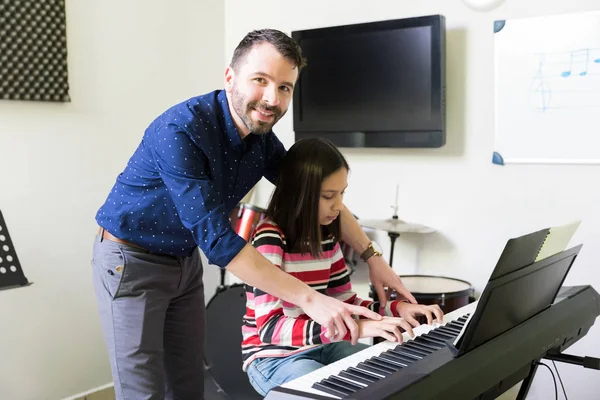音楽の授業で電子ピアノのメロディを演奏する女の子を助ける半ば大人講師 — ストック写真