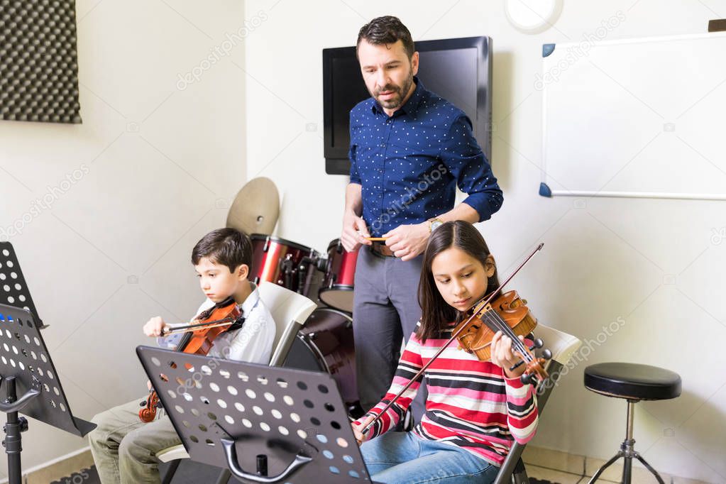 Professional teacher listening to music played by cute students in classroom