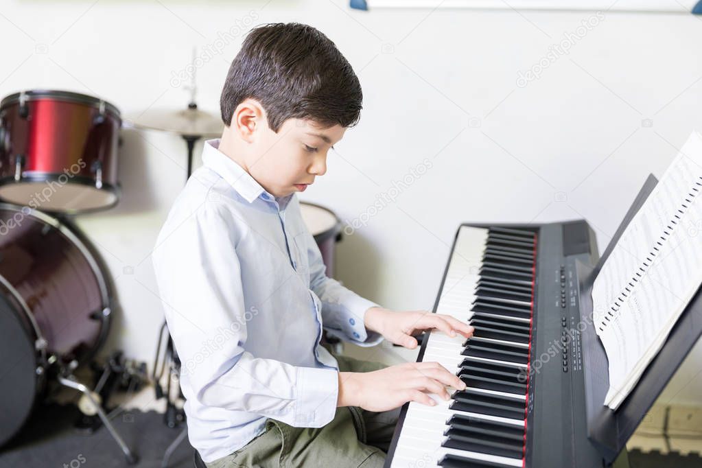 Student trying new melody on sound synthesizer in extracurricular session at school
