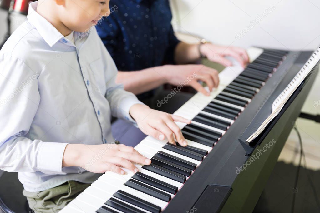 Midsection of boy learning to play electric piano from teacher in music class