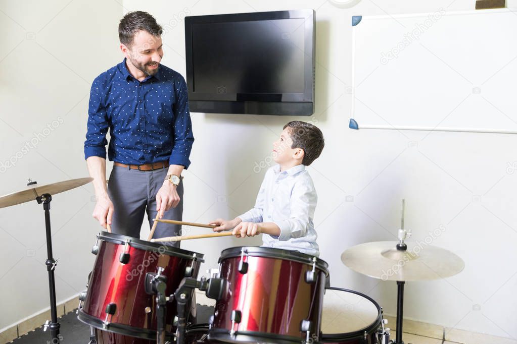 Smiling music teacher educating boy with his drum playing techniques
